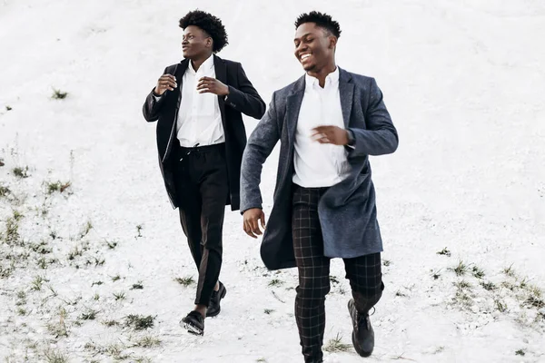 Havalı Afro-Amerikan kıvırcık saçlı, şık, benzer takım elbiseli adamlar, gün batımında kayalık bir bölgede moda pozu veriyorlar.