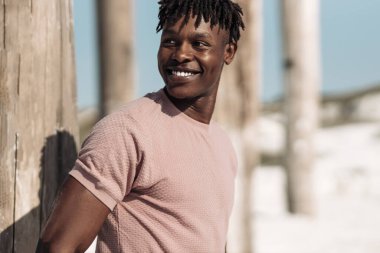 Afro saçlı, geniş gülümsemeli, açık havada gülen yakışıklı, mutlu bir Afrikalı adamın portresi.