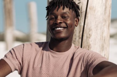 Mutlu siyah bir adamın portresi. Sıcak, geniş bir gülümsemesi var. Sıradan beyaz bir tişört giyiyor.