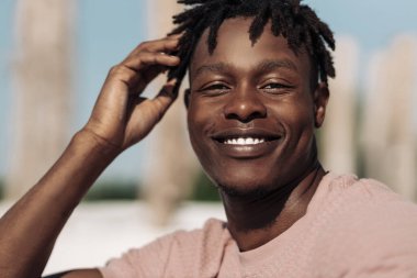 Yakışıklı, gülümseyen, kıvırcık saçlı, açık havada mutlu bir adam olan siyahi Afrikalı bir adamın yakın portresi.