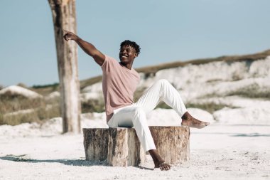 Yakışıklı gülümseyen mutlu Afrikalı tam gelişim, şık günlük kıyafetler içinde, yan tarafa bakıyor, kumsalda, moda konsepti, tarz, insanlar, çöl