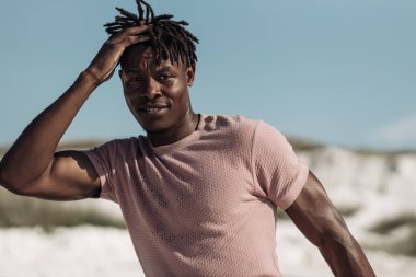 Yakışıklı, gülümseyen, kıvırcık saçlı, açık havada mutlu bir adam olan siyahi Afrikalı bir adamın yakın portresi.