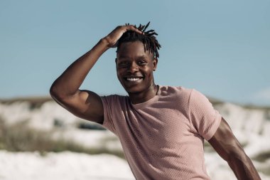 Yakışıklı, gülümseyen, kıvırcık saçlı, açık havada mutlu bir adam olan siyahi Afrikalı bir adamın yakın portresi.