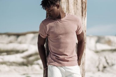 Tarz sahibi yakışıklı bir adamın açık bir portresi, şık kıyafetler içinde, kumda poz veren siyah bir adam, erkek moda konsepti.