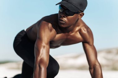 Formda ve kendinden emin Afro-Amerikan erkek, koşmaya hazır, erkek sporcu koşuya başlamak üzere, doğada, parlak güneş ışığı, spor konsepti, başlama, motivasyon