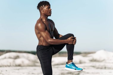 İyi esneme hareketleri yapan yakışıklı Afro-Amerikan erkek, doğada spor yaparken esneme hareketleri yapıyor.