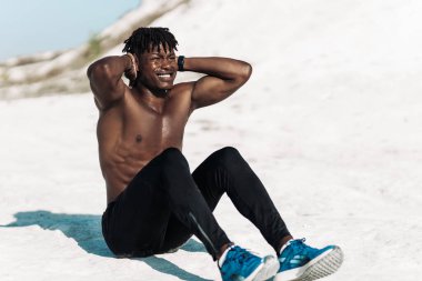 Atletik kaslı siyah adam, çıplak göğsü olan, karın egzersizi yapan, dışarıda yerde yatan karın kasları üzerinde çalışan fitness adamı.