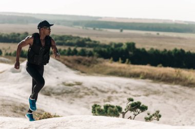 Afrika kökenli Amerikalı fitness erkekleri, spor kıyafetleriyle dağdaki kayalık yolda koşuyorlar, kaslı adam dağlara tırmanıyor.