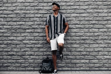 Sırt çantalı, kepli ve gömlekli yakışıklı Afrikalı bir adam.