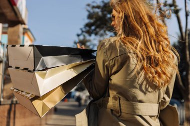 Alışveriş çantalarına yakın çekim ve kadının saçı çıkıyor. Kadınlar sokakta alışveriş torbaları, bej yağmurluk ve güneş gözlüğü takan kadınlar, mevsimlik alışveriş konsepti.