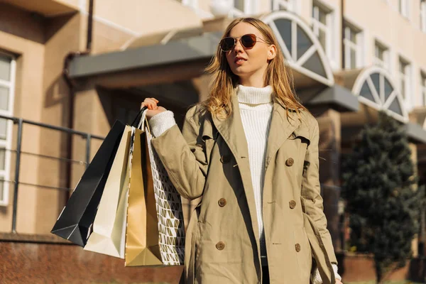 穿着米色雨衣 手里拿着太阳镜和购物袋的漂亮女人在商场购物 秋季大减价概念 春天购物 — 图库照片