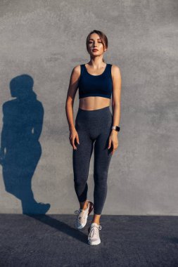 Spor kıyafetleri içinde spor spor yapan bir kadın gri beton arka plan, spor giyim ve açık hava ayakkabıları üzerinde yoga egzersizi yapıyor.