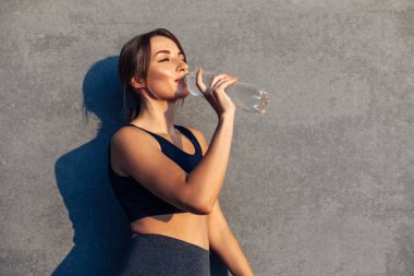Spor fitness kadını, yorucu bir koşudan sonra dinleniyor sporcu kadın idmandan sonra şehir duvarının izole edilmiş gri arka planında su içiyor.