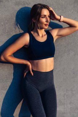 Güzel, gülümseyen sağlıklı bir fitness kadınının portresi, güzel bir atletik vücudu, spor kıyafetleri, spor sonrası mutlu kadın, arka planda gri bir şehir duvarı, konsept, spor, motivasyon