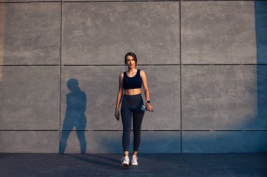 Spor kıyafetleri içinde spor spor yapan bir kadın gri beton arka plan, spor giyim ve açık hava ayakkabıları üzerinde yoga egzersizi yapıyor.