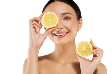 Doğal kaplıca. Güzel, genç, üstsüz bir kadın gözlerinin önünde portakal dilimleri tutuyor, yüzünün yanında turuncu yarımlar tutuyor, beyaz arka planda sulu turuncu bir yüzü olan güzel bir kadın.