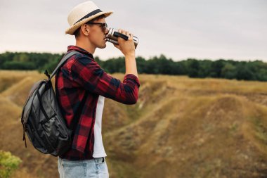 Sırt çantalı bir yürüyüşçü dağın tepesinde oturur ve kıyı manzarasının tadını çıkarır. Elinde bir fincan kahveyle bir kayanın üzerinde oturan genç bir adam çevresindeki doğa manzarası ile birlikte. Dağ ve sahil yolculuğu