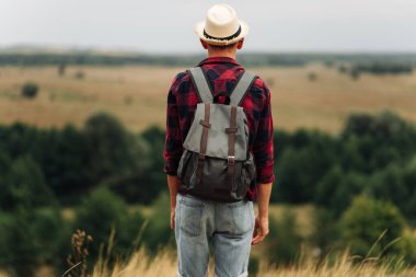 Sırt çantalı, güneş gözlüklü ve şapkalı bir yürüyüşçü dağın tepesinden vadinin manzarasının tadını çıkarıyor. Mutlu turist vadide yürüyor. Seyahat ve macera konsepti
