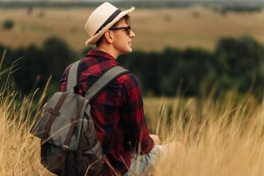Sırt çantalı, güneş gözlüklü ve şapkalı bir yürüyüşçü dağın tepesinden vadinin manzarasının tadını çıkarıyor. Mutlu turist vadide yürüyor. Seyahat ve macera konsepti