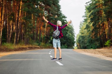 Sırt çantalı gezgin adamın elleri güneşin doğuşuna doğru uzanıyor, özgürlük ve hayatın tadını çıkarıyor. Şapkalı bir adam otobanın ortasında duruyor ve ormanın temiz havasının tadını çıkarıyor.