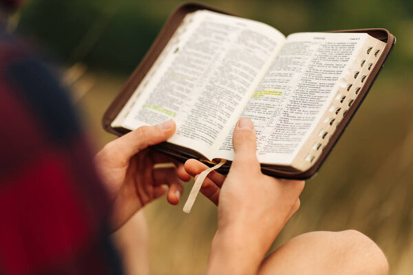 Reading the Bible outdoors in nature. A man in sunglasses and a shlap holds a Bible in his hands, standing in the forest. Faith, spirituality and religion concept