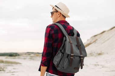 Arkaya bakan, şapkalı gezgin, ellerini dağın tepesindeki patikaya kaldırıyor, arkadan bakıyor. Yüksek kayalıkların tepesinde bir turist. Özgürlük, seyahat, zafer konsepti