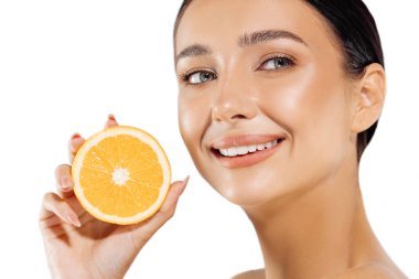 Kadın ve meyve portresi. Mutlu bir manken yüzüne yakın sulu bir portakal tutar ve beyaz arka plandaki kameraya bakar. Güzel bir kız sağlıklı cilt için narenciye ve doğal vitaminler kullanır.