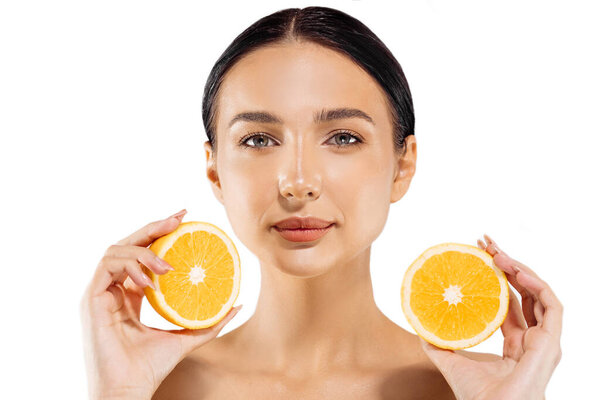 Woman and fruit portrait. A happy model holds a juicy orange near her face and looks at the camera on a white background. Beautiful girl uses citrus fruits and natural vitamins for healthy skin