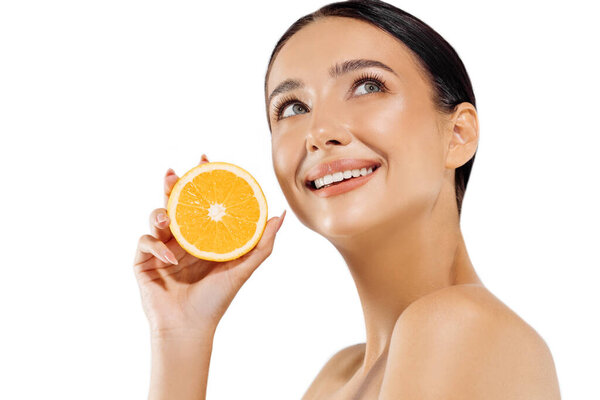 Woman and fruit portrait. A happy model holds a juicy orange near her face and looks at the camera on a white background. Beautiful girl uses citrus fruits and natural vitamins for healthy skin