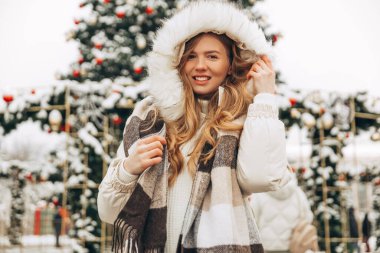 Happy beautiful woman with long hair, in a warm winter jacket and scarf, posing on the street of the city. Christmas, winter holidays concept. Snowfall