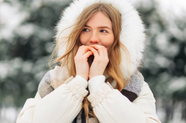 Happy girl warming up her hands in warm winter clothes. Attractive model portrait outdoors on a cold day. Freezing a woman outside