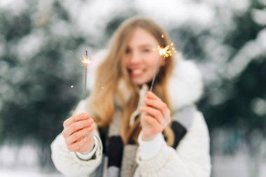 Charming woman in warm winter clothes posing with sparklers on the street in winter. Gorgeous woman holding sparklers and laughing in the new year