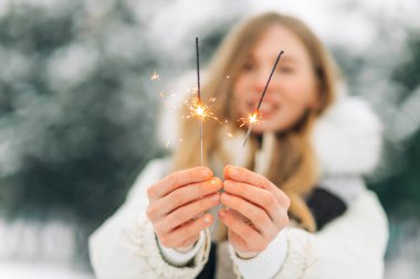 Holidays and celebration concept. Close-up of excited woman with sparklers in hands, outdoors in winter snowy weather, looking at camera happy