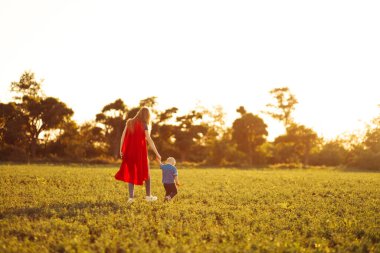 Parkta süper kahraman kostümleri içinde koşan mutlu anne ve oğulun panoramik çekimi. Anne ve oğlu süper kahraman kostümleri içinde. Anne ve bebek eğleniyor, gülümseyin. Aile kavramı