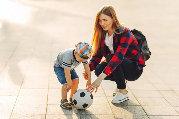 Happy family play football in summer, Mother and son play and run in the park on a beautiful morning. A boy kicks football while playing with his family. Family concept