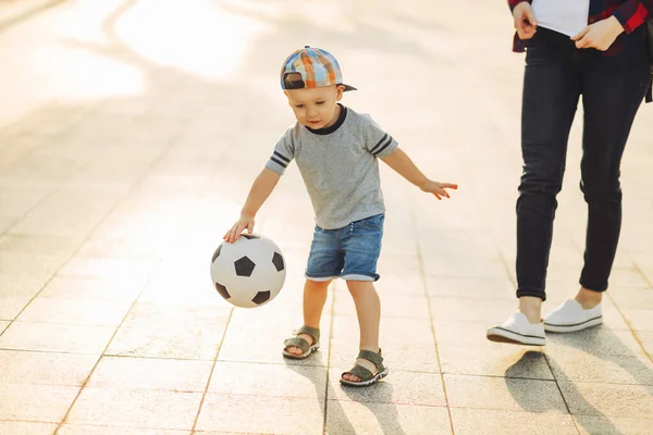妈妈和儿子一起在公园外面踢足球 小男孩踢足球 孩子学习踢足球 家人一起在公园踢足球 — 图库照片