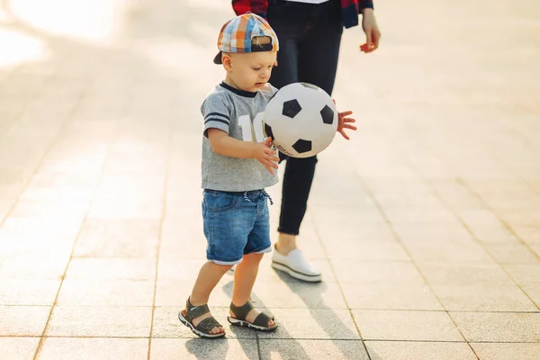 Mom and son play football together outdoors in the park, Little boy kicks a soccer ball, child learns to play football. Family playing football together in the park