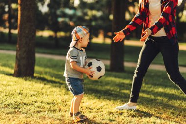 Mutlu bir aile. Güneşli bir yaz gününde anne ve oğlu çimlerin üzerinde futbol oynarken eğleniyorlar. Anne ve çocuk parkta oynuyorlar. Aile parkta futbol oynuyor, Anneler Günü.