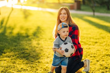 Mutlu bir aile. Güneşli bir yaz gününde anne ve oğlu çimlerin üzerinde futbol oynarken eğleniyorlar. Anne ve çocuk parkta oynuyorlar. Aile parkta futbol oynuyor, Anneler Günü.