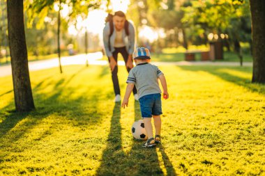 Yeşil bir parkta futbol topu olan bir baba ve oğul. Futbol sahasında baba oğul aktivitesi. Yaz konsepti. Aile yazın çocuklarıyla futbol oynuyor.