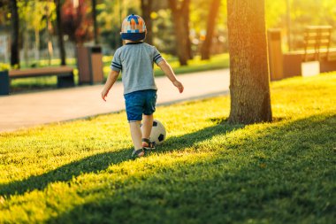Parktaki yeşil çimlerin üzerinde sokak futbolu oynarken küçük çocuk topa vuruyor. Çocuklar için doğa sporları. Gelişim konsepti, çocuklar için aktif eğlence, spor
