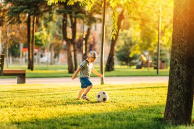 Güneşli bir günde futbol sahasında futbol oynayan küçük bir çocuğun yakın çekimi. Anaokulu çocuklarının sağlıklı boş vakitleri
