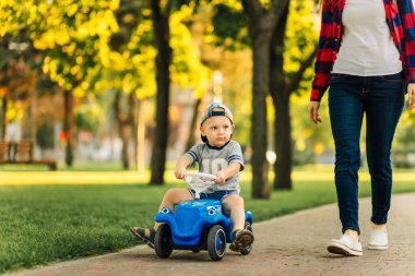 Anne oğluna parkta oyuncak araba sürmeyi öğretiyor. Anaokulu öğrencisi yazın oyuncak arabasını dışarıda kullanıyor. Mutlu aile, çocukluk konsepti, açık hava eğlencesi