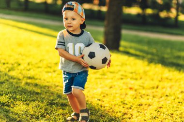 Güneşli bir günde futbol sahasında futbol oynayan küçük bir çocuğun yakın çekimi. Anaokulu çocuklarının sağlıklı boş vakitleri