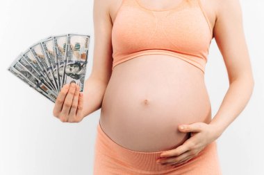 Hamile bir kadın beyaz bir arka planda elinde banknotlar tutuyor. Gebelik ve doğum masrafları. Hamilelik ve taşıyıcı annelik kavramı. Elinde dolar tutan hamile bir kadın.
