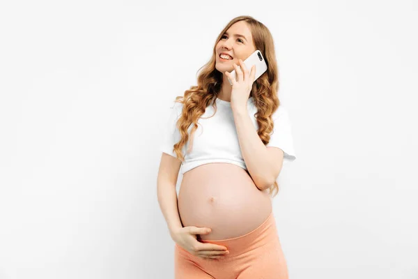 Phone call. Smiling beautiful pregnant woman talking on a mobile phone, consulting a doctor, on an isolated white background with free space