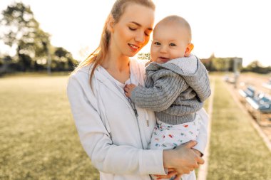 Anneler Günü. Sevimli küçük oğlu olan sevimli, genç bir anne. Sevgi dolu bir aile. Anne ve bebek dışarıda oynuyor, öpüşüyor ve sarılıyorlar. Anneler Günü, 8 Mart, aile tatili ve birliktelik kavramı..