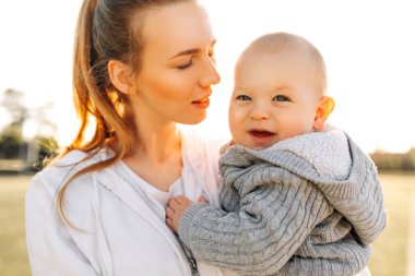 Anneler Günü. Sevimli küçük oğlu olan sevimli, genç bir anne. Sevgi dolu bir aile. Anne ve bebek dışarıda oynuyor, öpüşüyor ve sarılıyorlar. Anneler Günü, 8 Mart, aile tatili ve birliktelik kavramı..