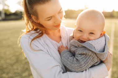 Mutlu genç anne sıcak bir ilkbahar ya da yaz gününde oğluyla oynuyor ve onunla eğleniyor. Bahçede ya da parkta güzel bir gün batımı ışığı. Mutlu Aile Konsepti, Anneler Günü, 8 Mart