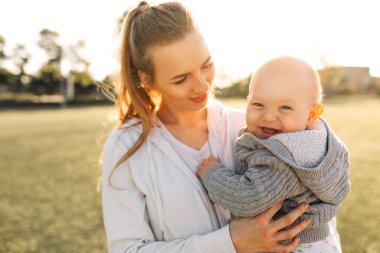 Aile, çocuklar ve mutlu insanlar konsepti. Mutlu anne dışarıda oynar, sarılır ve oğlunu öper. Mutlu kadınlar günü. Aile tatili ve birlik.